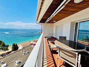 Uma varanda com vista para o mar, uma mesa e cadeiras.