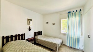 Een slaapkamer met twee bedden, een raam met gordijnen, een nachtkastje en een wandlamp.