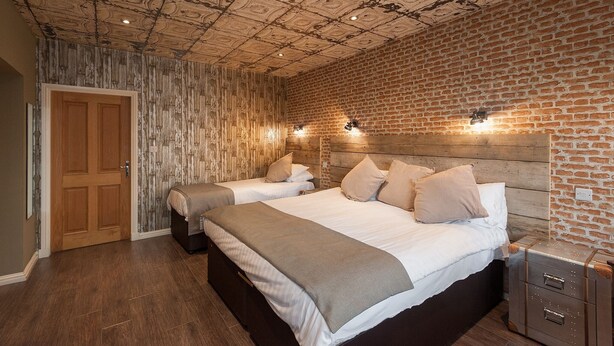 A bedroom with two beds, a wooden headboard, a brick wall, and a wooden ceiling. - Chic Designed Themed  Apartment In The Edinburgh City Centre (Edinburgh)