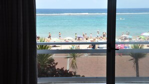 Vista desde una ventana hacia una playa con gente y sombrillas.