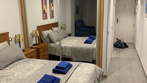 Habitación de hotel con dos camas, un espejo grande y un pasillo que conduce a otra habitación.