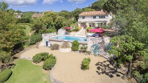 Une grande maison avec une piscine, entourée d’un jardin bien entretenu et d’arbres.