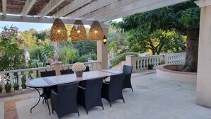 Une terrasse extérieure avec une table ronde et des chaises, entourée de plantes en pot et d’une rambarde.