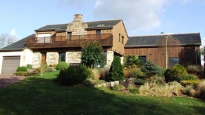 Ein zweistöckiges Haus mit einer Stein-Fassade, einem Holz-Anbau und einem gepflegten Rasen.