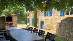 Un espacio de comedor al aire libre con un muro de piedra, un horno de ladrillo y contraventanas azules en un edificio.