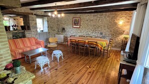 Una habitación rústica con suelo de madera, paredes de piedra, una mesa de comedor con sillas, un sofá y una pequeña mesa blanca.