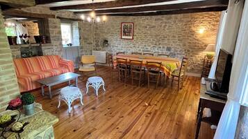 A rustic room with a wooden floor, stone walls, a dining table with chairs, a sofa, and a small white table.