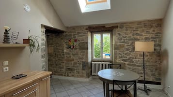A spacious room with a skylight, stone walls, a dining table, and a kitchen area.