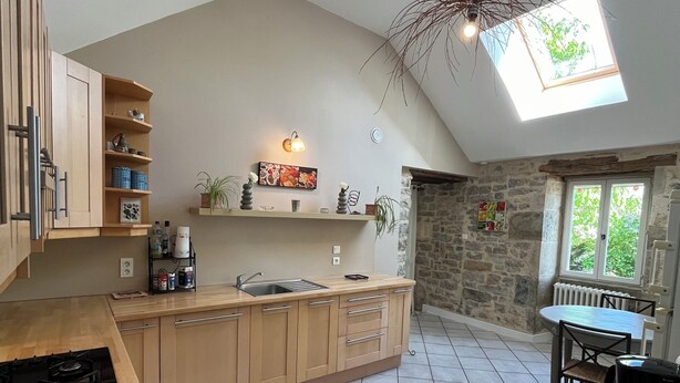 Una cocina con una isla central, un área de comedor con mesa y sillas, una pared de piedra y un tragaluz.