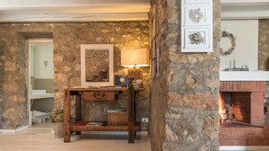 Una habitación de paredes de piedra con chimenea, una mesa de madera con una lámpara y un cuadro enmarcado en la pared.