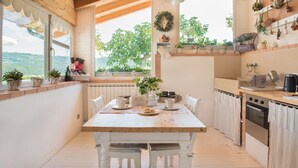 Una cocina con una mesa de madera, sillas blancas, un horno de ladrillo y plantas en macetas.