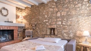 Un dormitorio con pared de piedra, chimenea, cama con ropa de cama floral y mesita de noche con lámpara.