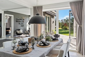 A dining area with a table set for four, a large pendant light, and a view of a garden through glass doors. - Modern house 15 min from Center of Stockholm (Boo)