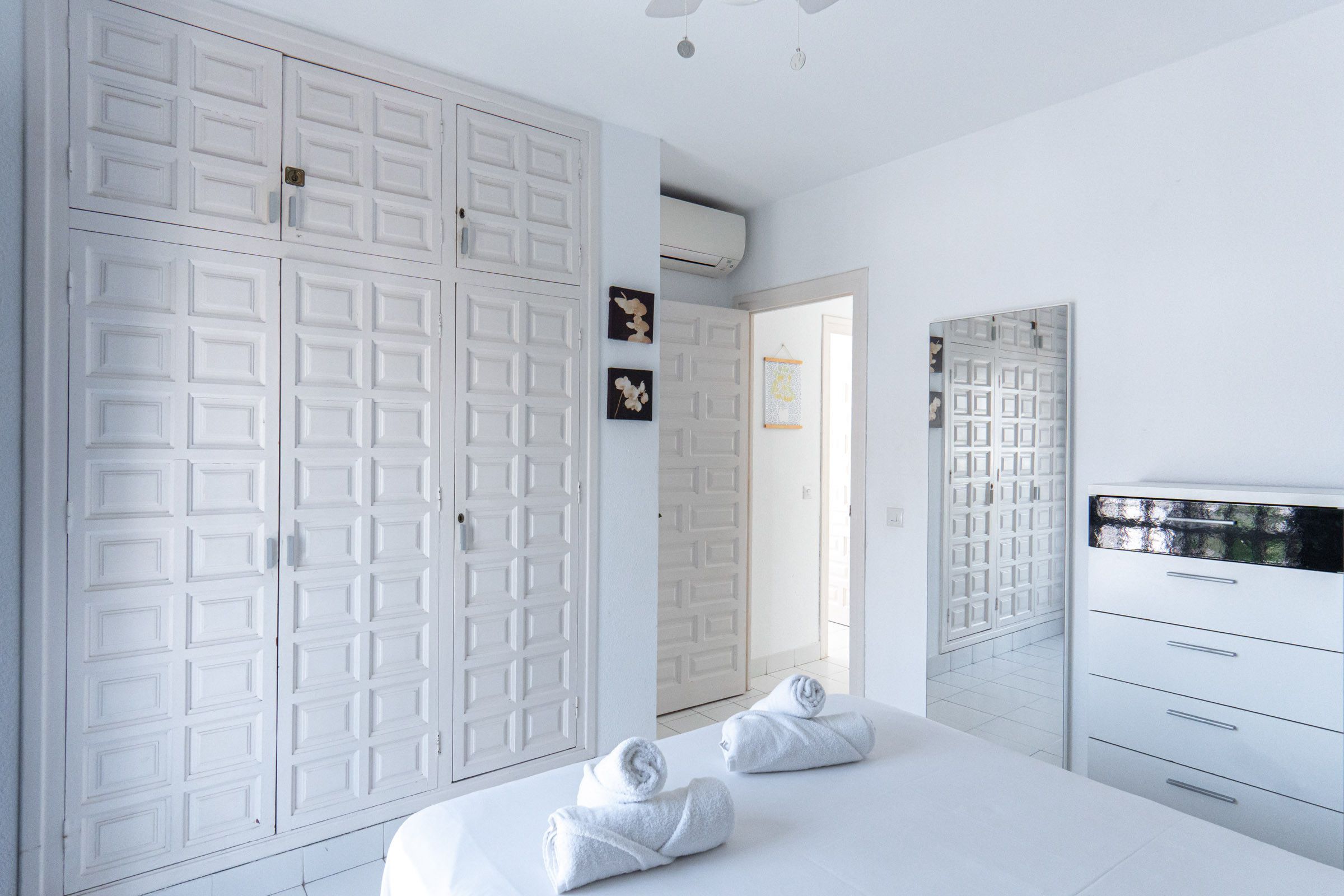 A hotel room with a large wardrobe, a bed with towels, a dresser, and a mirror. - Los Pinos 25 Villas by Casasol (Nerja)