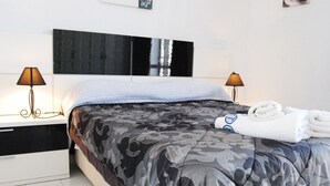 Een net opgemaakt bed met een spreidekbed met camouflageprint, twee bedlampen en een opgevouwen handdoek op het bed.