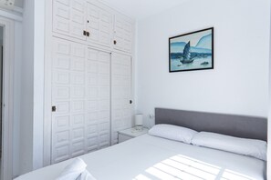 A bedroom with a bed, a nightstand, a white wardrobe, and a painting on the wall.