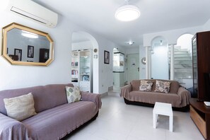 A living room with two sofas, a small table, and a TV stand. There is a bookshelf and a mirror on the wall.