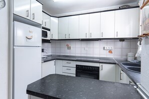 A compact kitchen with white cabinets, a black countertop, and a built-in dishwasher.
