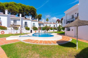 A pool area with a circular design, surrounded by white buildings with red-tiled roofs, and a thatched umbrella. - Los Pinos 25 Villas by Casasol (Nerja)