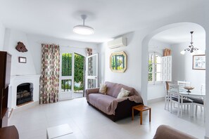 A living room with a sofa, a small table, a fireplace, and a dining area with chairs and a table. - Los Pinos 25 Villas by Casasol (Nerja)