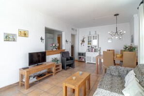 Un salon comprenant un canapé, un téléviseur, une table basse en bois et un coin repas avec des chaises et une table.