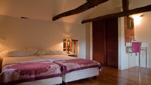 A bedroom with a double bed, a bedside table with a lamp, wooden beams on the ceiling, and a wooden door.