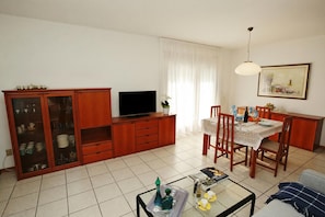 Sala de estar com televisão, armário de madeira, mesa de jantar, cadeiras e sofá.