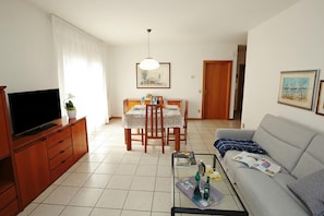 Uma sala de estar com televisão, sofá, mesa de centro, mesa de jantar e cadeiras.