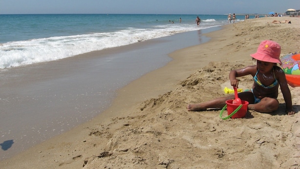 Ein sandiger Strand mit einem Kind, das mit Spielzeug und Eimer spielt.