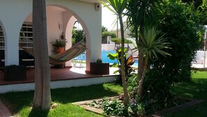 Eine Terrasse mit einer Hängematte, einem Pool und einem Garten.