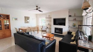 A living room with a sofa, a dining table with chairs, a TV, a fireplace, and a ceiling fan.