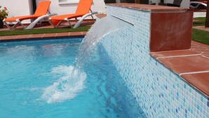 Ein Pool mit Wasserspiel, orangefarbenen Liegestühlen und einer gefliesten Liegefläche.