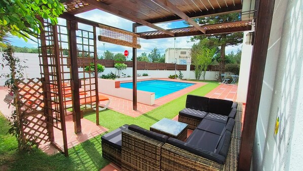 A covered outdoor area with a pool, seating, and a pergola.