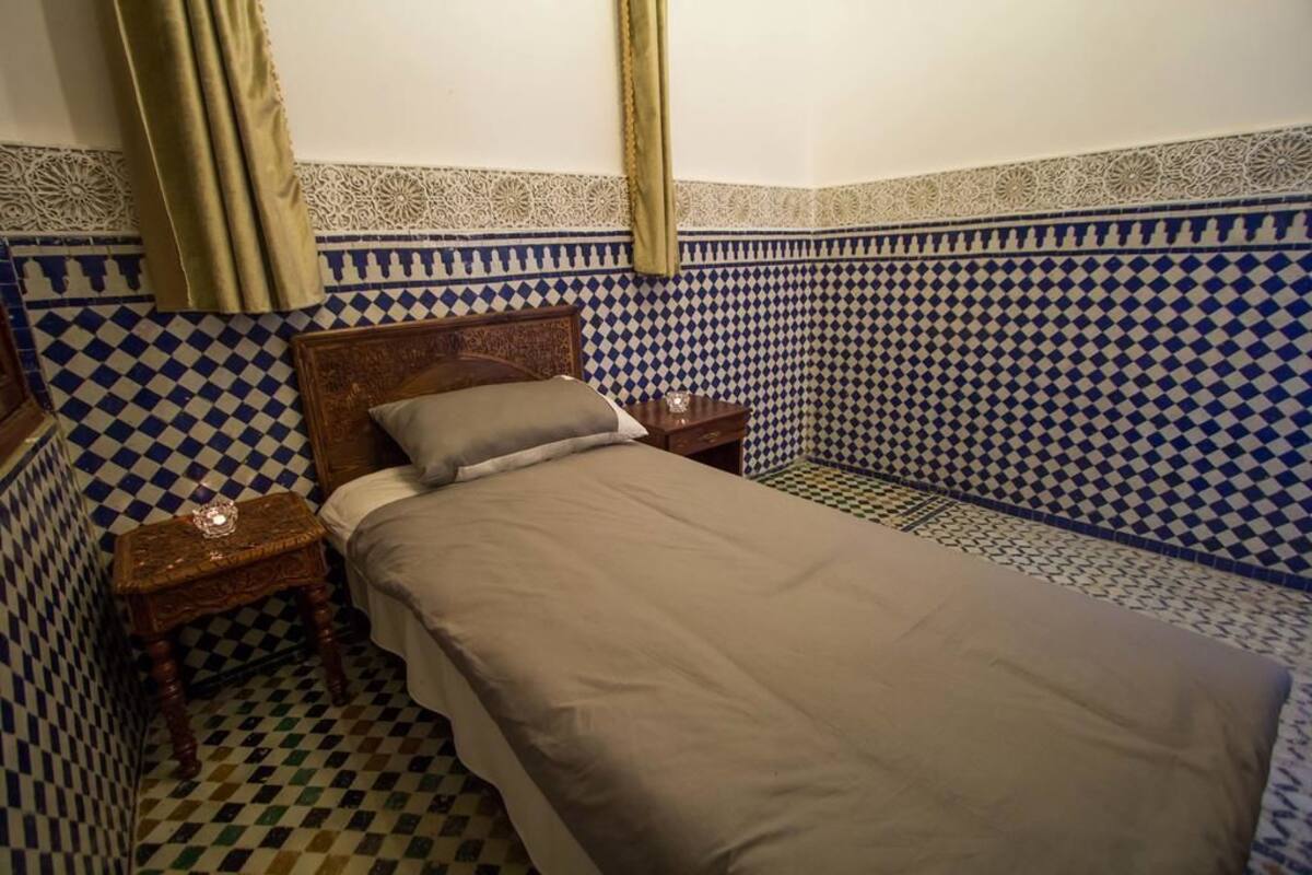 Una habitación pequeña con cama individual, suelo a cuadros y paredes con diseño.