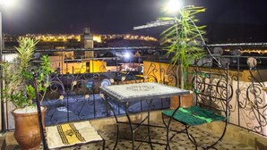 A rooftop terrace with a table and chairs, potted plants, and a view of a cityscape at night. - Dar el Mathaf (Fes)