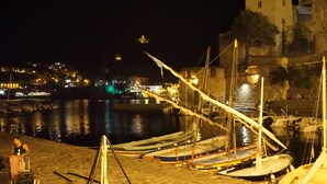 A nighttime harbor with boats docked, a stone building in the background, and a person standing by the water. - Apartment/ flat - COLLIOURE (Collioure)