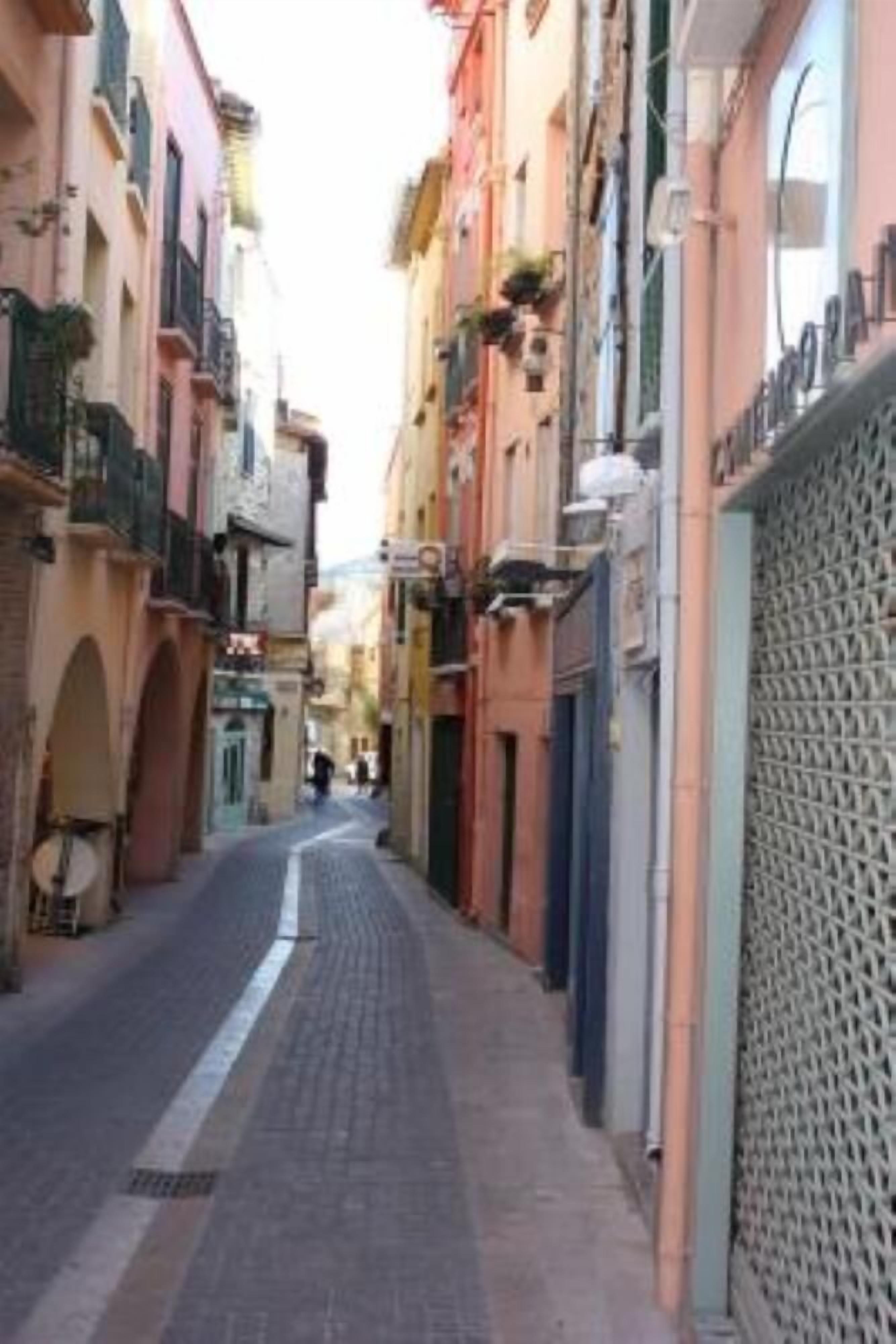 A narrow street lined with colorful buildings, a cobblestone path, and a lattice fence on the right.