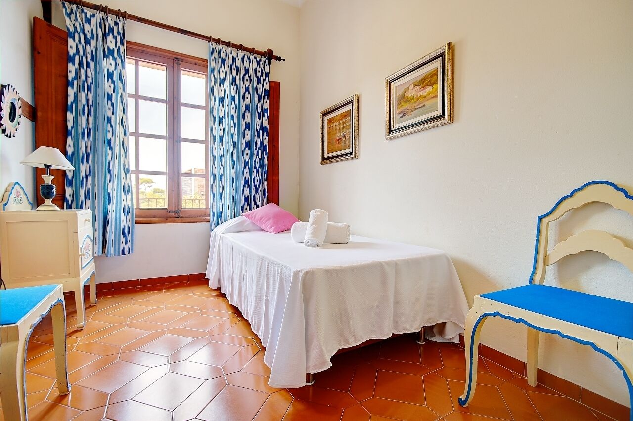 Een slaapkamer met een bed, een stoel, een tafel en een raam met gordijnen.