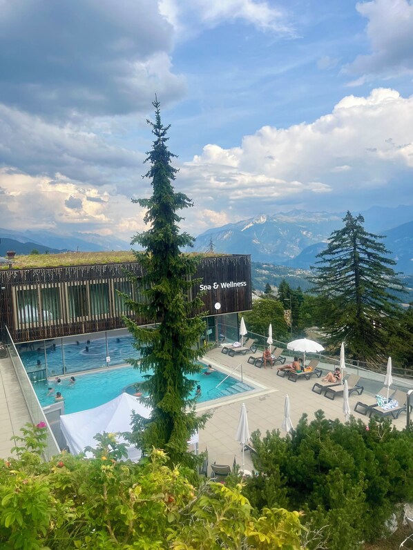 A pool area with lounge chairs and umbrellas, surrounded by trees and a mountain view.
