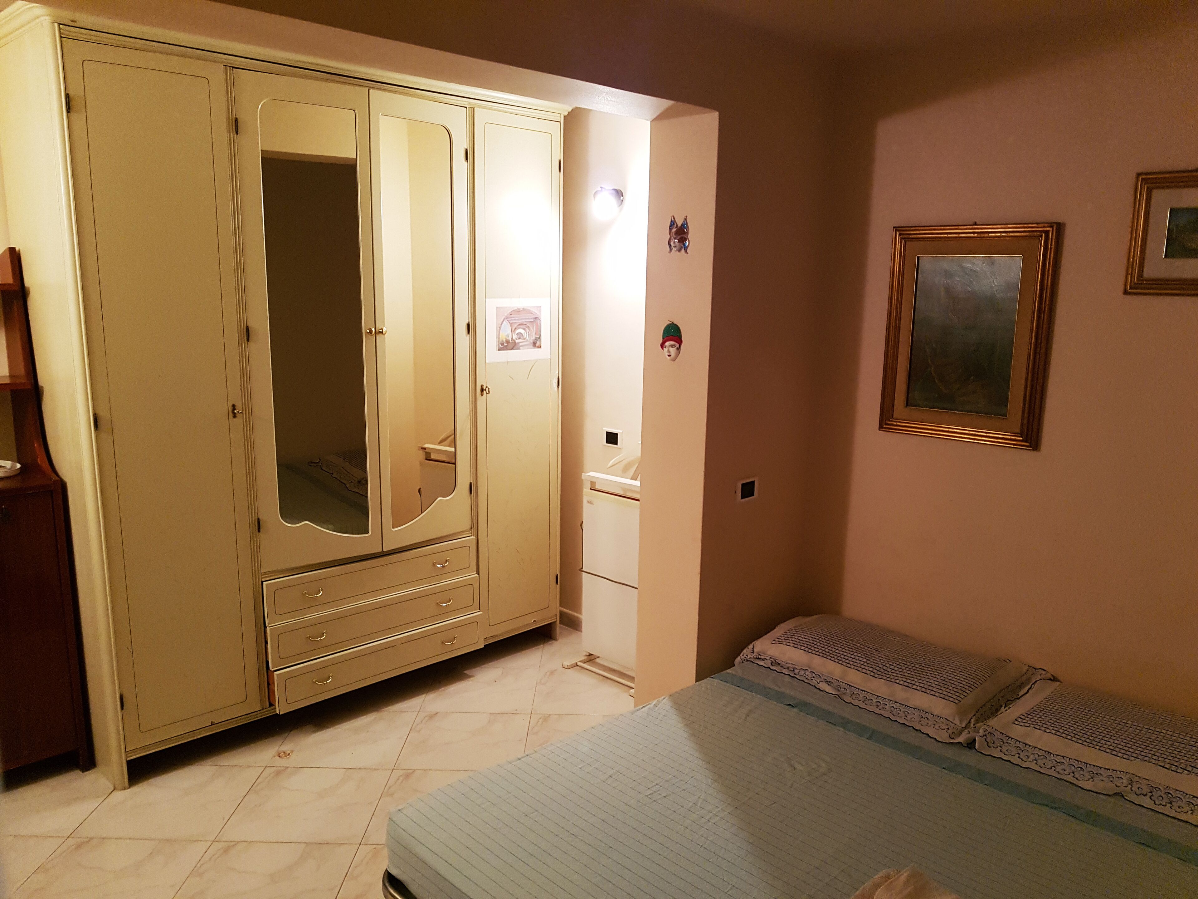 Un dormitori amb un armari ampli, un llit amb roba de llit estampada, una petita taula de nit i un quadre al mur.