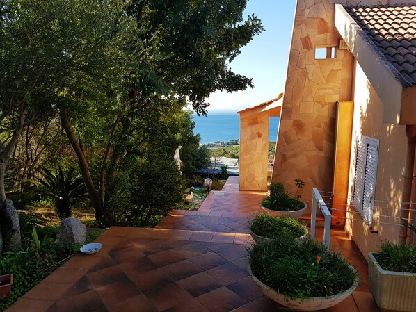 A pathway leading to a building with stone walls and a view of the sea.