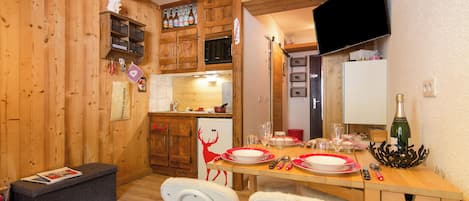 Un intérieur en bois comprenant une table à manger pour deux personnes, un réfrigérateur et des placards en bois.