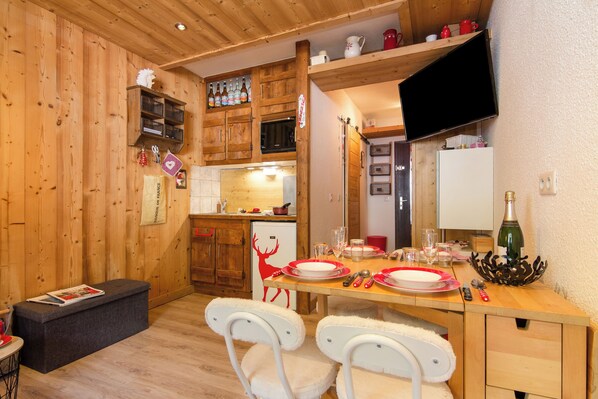 A wooden interior with a dining table set for two, a refrigerator, and wooden cabinets.