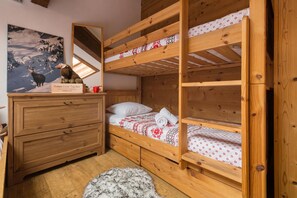 A wooden bunk bed with a red and white patterned bedspread, a wooden dresser, a mirror, and a painting of deer on the wall.
