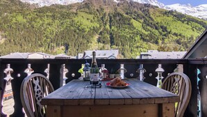 Ein Holztisch mit Flasche, Glas und Gebäck auf einem Balkon mit Blick auf einen Berg.