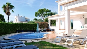 Una piscina con lettini e un edificio bianco con tetto in tegole.