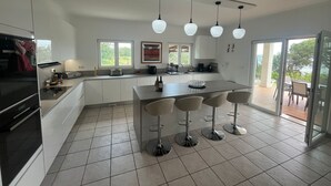 Una cucina moderna con isola centrale, sgabelli da bar e vista attraverso una porta in vetro.