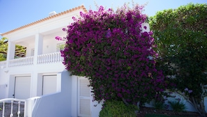 Un edificio bianco con un balcone, una recinzione bianca e un giardino con fiori viola.