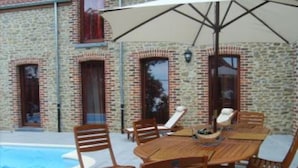 A stone building with a pool, wooden outdoor furniture, and a large umbrella.