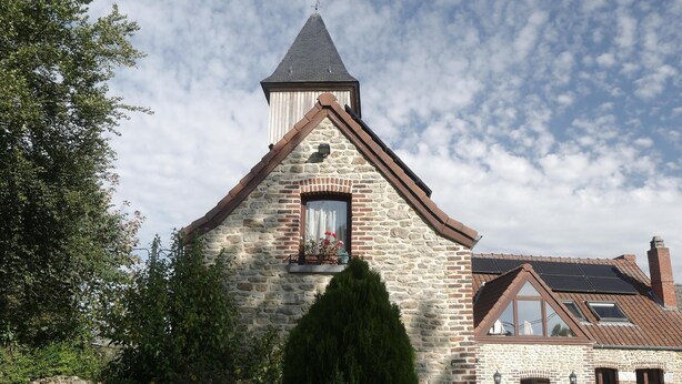 A stone building with a steeply pitched roof, a small window with a flower box, and a clear sky.